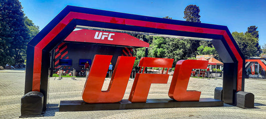 Outdoor brand activation with a giant red UFC letter installation under a branded archway on a sunny plaza