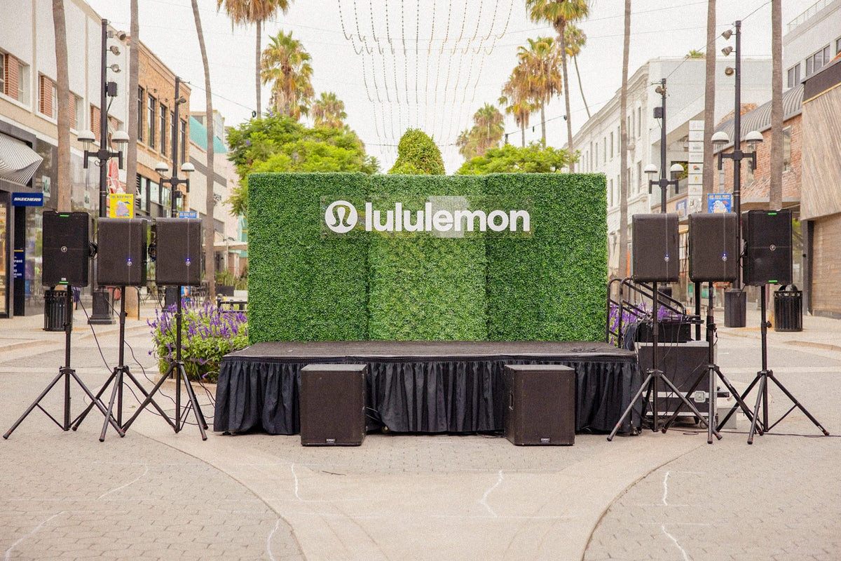 Lululemon outdoor event stage with speakers and greenery in a palm-lined shopping area